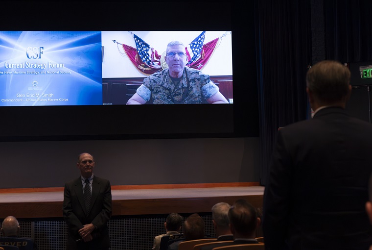 People in an auditorium, with a video guest in the background