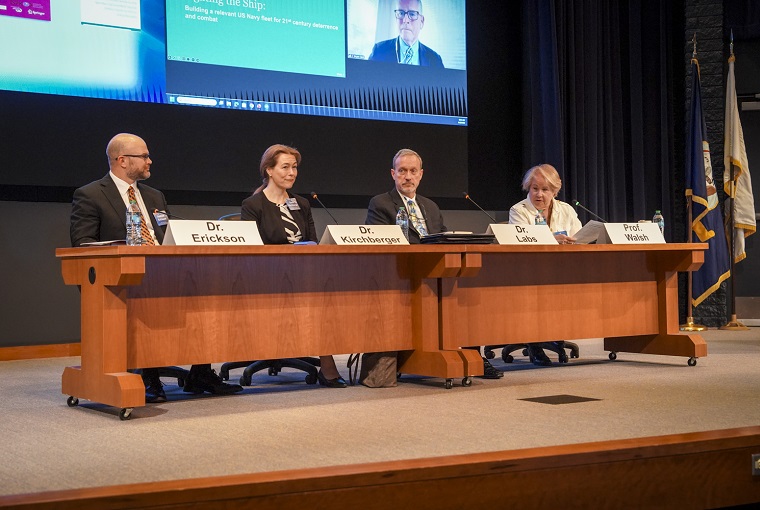 Four people at a conference table at a sympoium