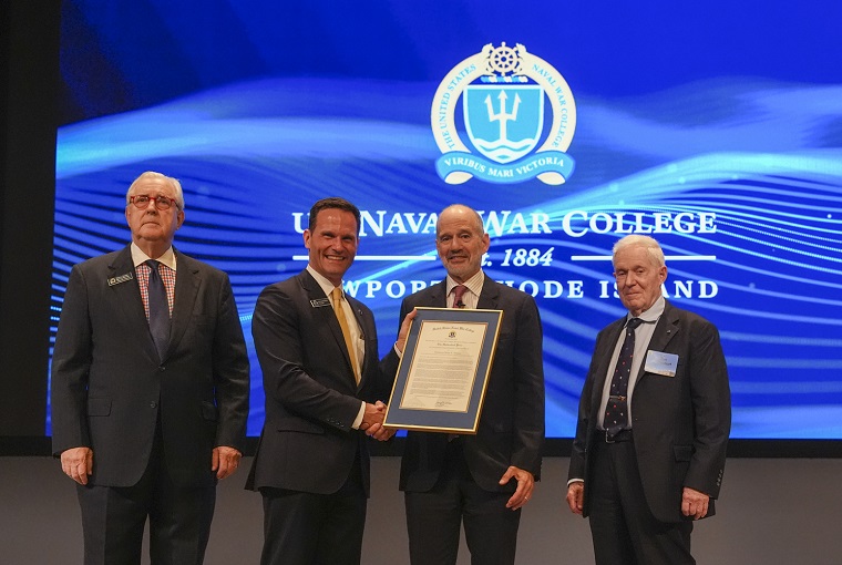 Four men on stage, one is receiving an award