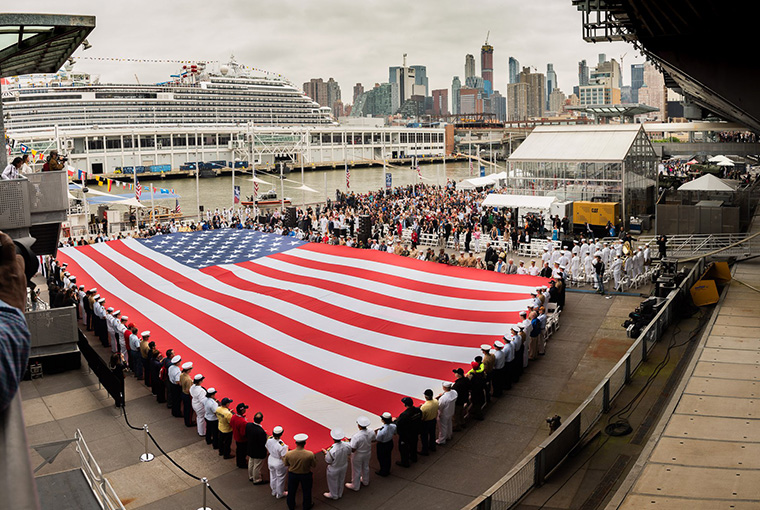 Navy Band Northeast performs 'America the Beautiful' while a flag is unfurled during the 2018 Memorial Day Observance ceremony on board the USS Intrepid.