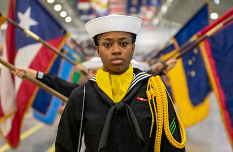 A performance division recruit leads the state flag performers inside Midway Ceremonial Drill Hall during a pass in review graduation ceremony at Recruit Training Command. 